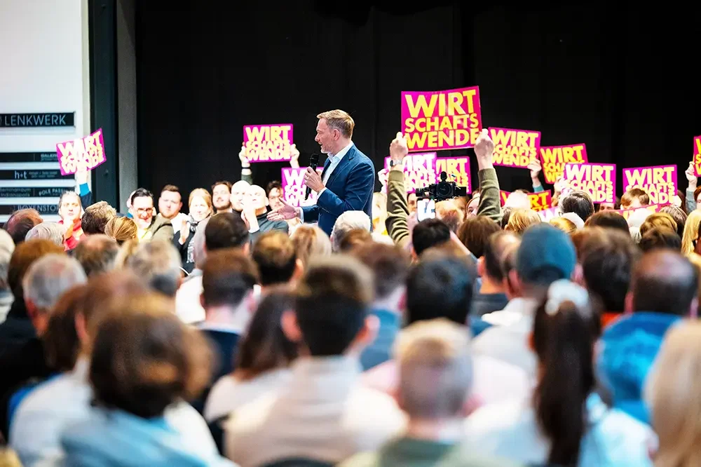 Christian Lindner spricht umgeben von Gästen die Schilder mit der Aufschrift 